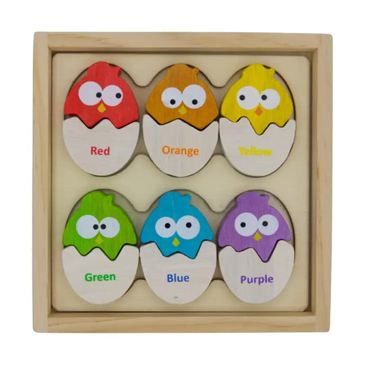 Six wooden egg puzzle pieces sit in a wooden box. Each egg is made of two pieces, one is white and labeled with the name of a color, the other half is painted in that color.