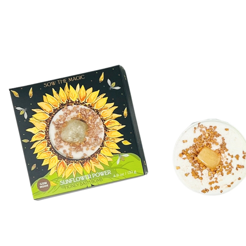 Product box showing a sunflower with honeybees flying around. Next to it is a bath bomb with gold flakes and a gemstone in the center.